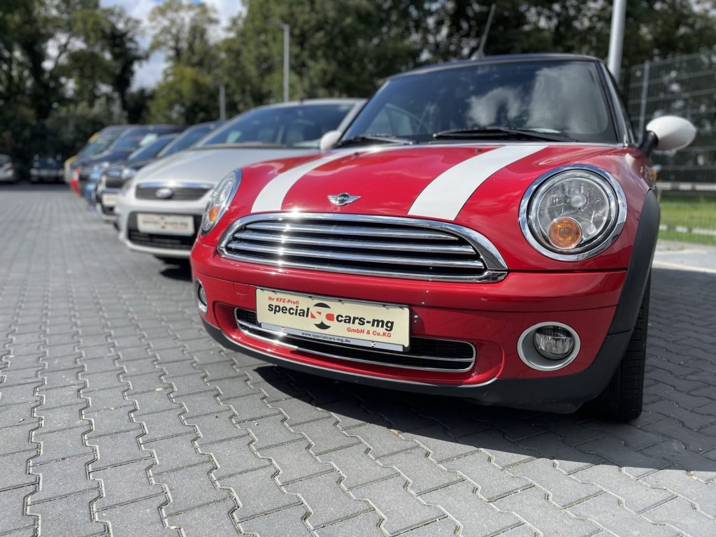 Eine Reihe von Autos auf einem Parkplatz, mit einem markanten roten Mini Cooper im Vordergrund mit auffälligen weißen Rennstreifen.
