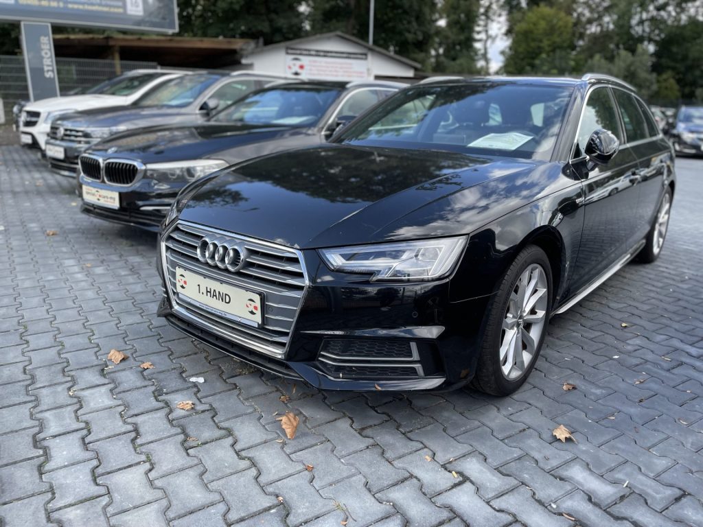 Auf einem Autoparkplatz steht ein schwarzer Audi A4, im Hintergrund sind mehrere andere Fahrzeuge zu sehen.