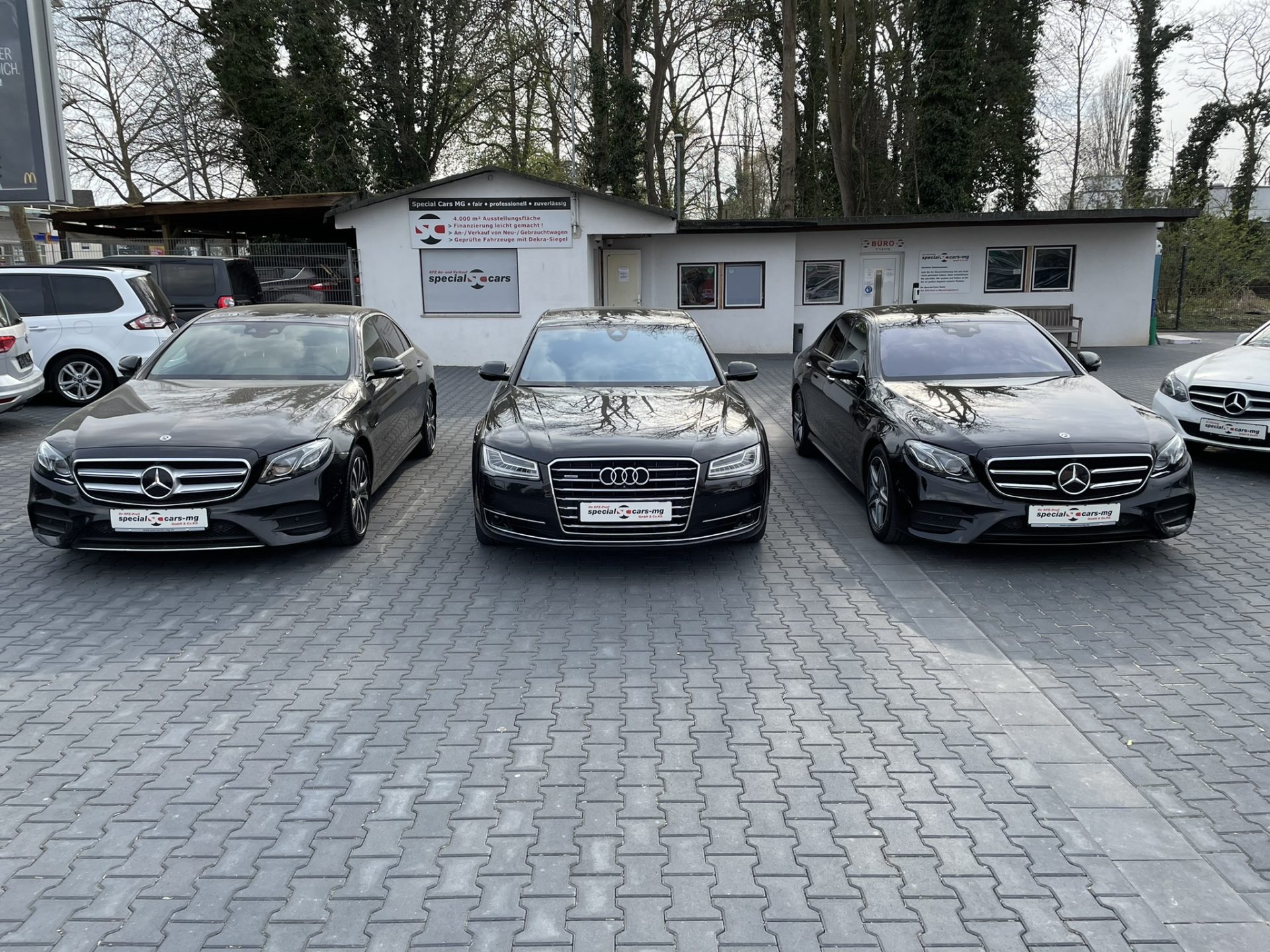 Drei schwarze Luxusautos parken in einer Reihe: links eine Mercedes-Limousine, in der Mitte ein Audi und rechts ein weiterer Mercedes.
